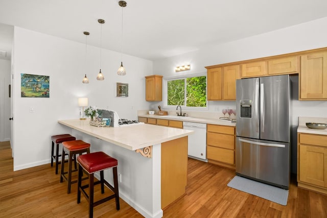 kitchen with a breakfast bar, light countertops, white dishwasher, a sink, and stainless steel fridge