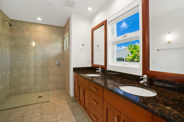 bathroom with dual vanity, tiled shower, and tile patterned flooring