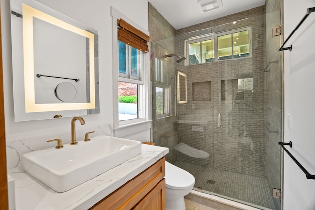 bathroom with toilet, a wealth of natural light, a shower with shower door, and vanity