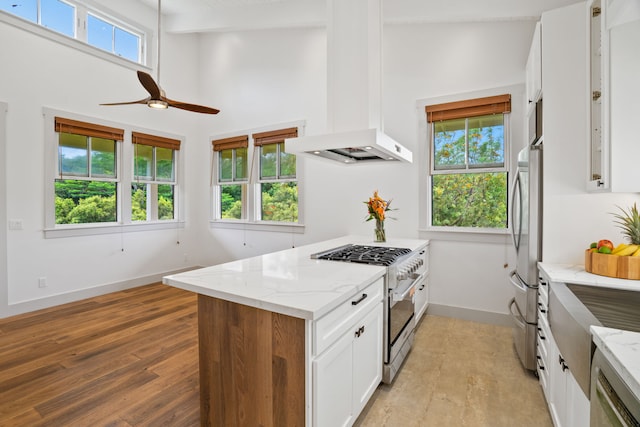 kitchen with white cabinets, appliances with stainless steel finishes, premium range hood, light stone counters, and light hardwood / wood-style flooring