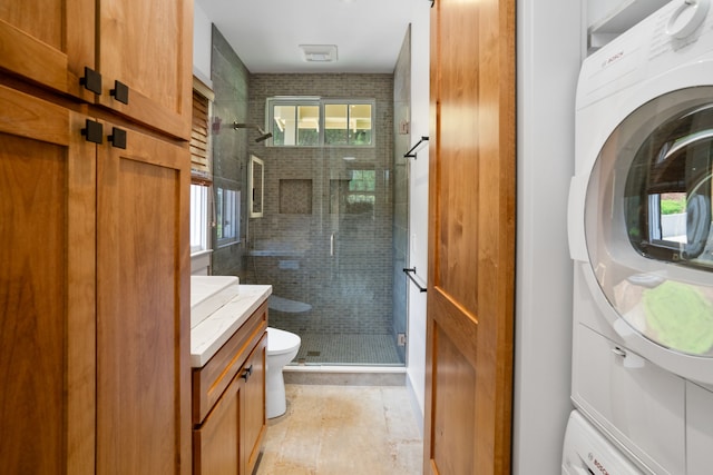 bathroom featuring toilet, a shower with door, stacked washer and dryer, and vanity