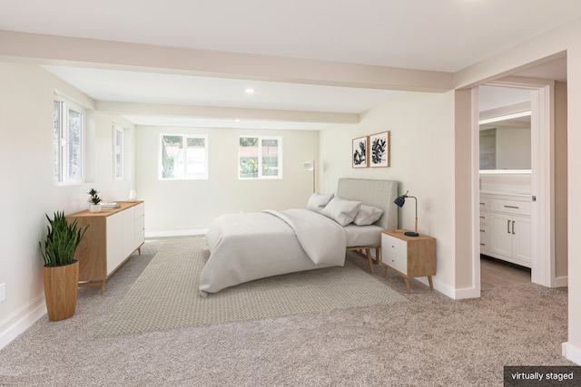 bedroom featuring beamed ceiling, connected bathroom, and light colored carpet