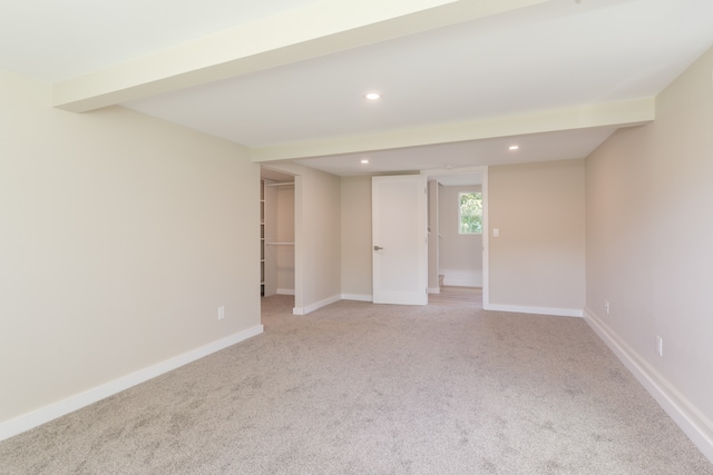 spare room featuring beamed ceiling and light colored carpet