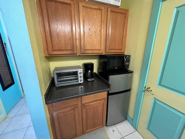 kitchen featuring freestanding refrigerator, black microwave, brown cabinets, and light tile patterned floors