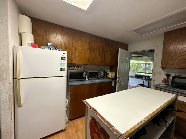 kitchen with light wood-type flooring, a kitchen island, and white fridge