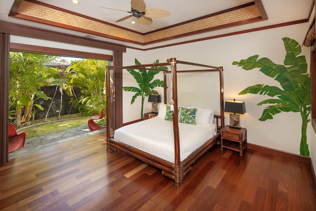 bedroom with ceiling fan, a tray ceiling, dark wood-type flooring, and ornamental molding