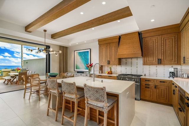 kitchen with pendant lighting, a center island with sink, appliances with stainless steel finishes, custom range hood, and an inviting chandelier