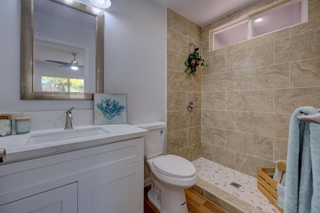 full bath featuring a tile shower, toilet, vanity, and wood finished floors