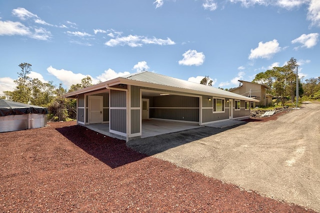 back of house with metal roof, an attached carport, dirt driveway, and a sunroom