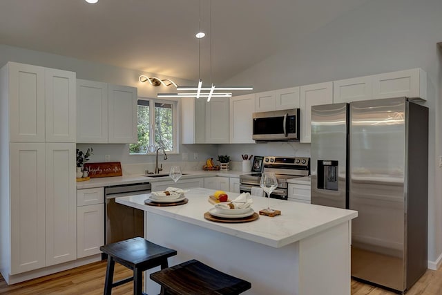 kitchen featuring a breakfast bar, a sink, white cabinetry, stainless steel appliances, and vaulted ceiling