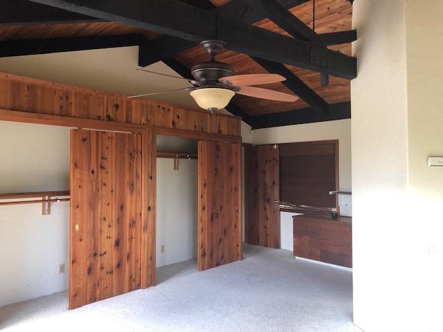 interior space with vaulted ceiling with beams, ceiling fan, carpet, and two closets