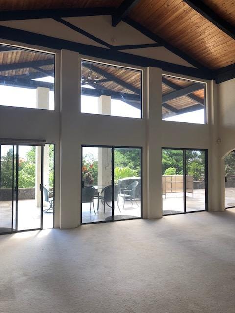 unfurnished living room featuring wooden ceiling, carpet, high vaulted ceiling, and beam ceiling