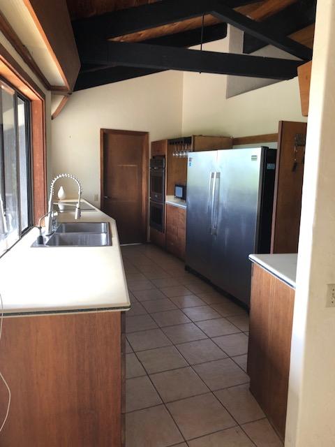 kitchen with lofted ceiling with beams, light tile patterned floors, a sink, brown cabinets, and black appliances