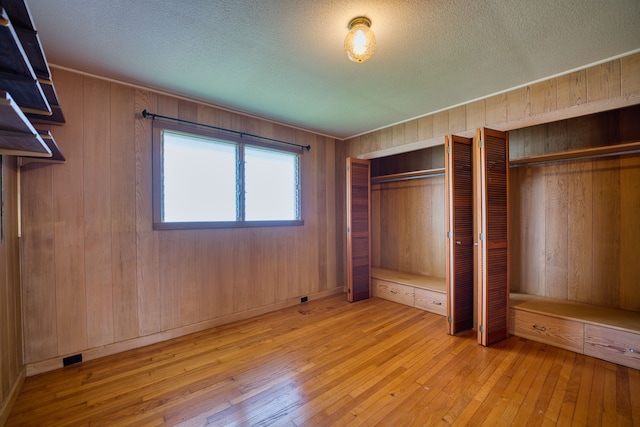 unfurnished bedroom with wooden walls, a textured ceiling, and light hardwood / wood-style flooring