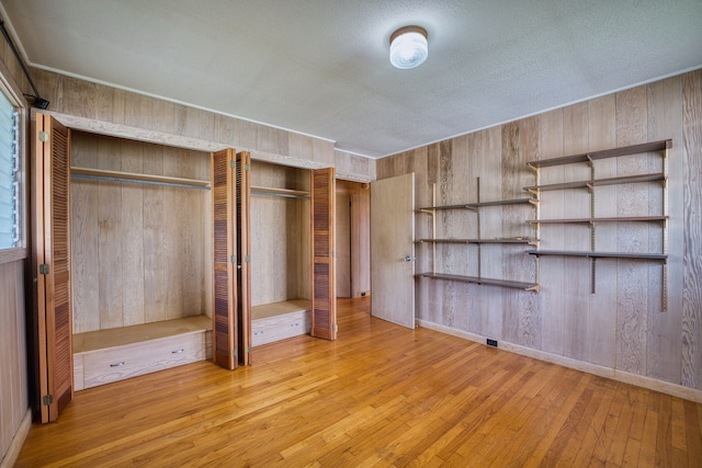 unfurnished bedroom featuring wooden walls, a textured ceiling, and light hardwood / wood-style floors