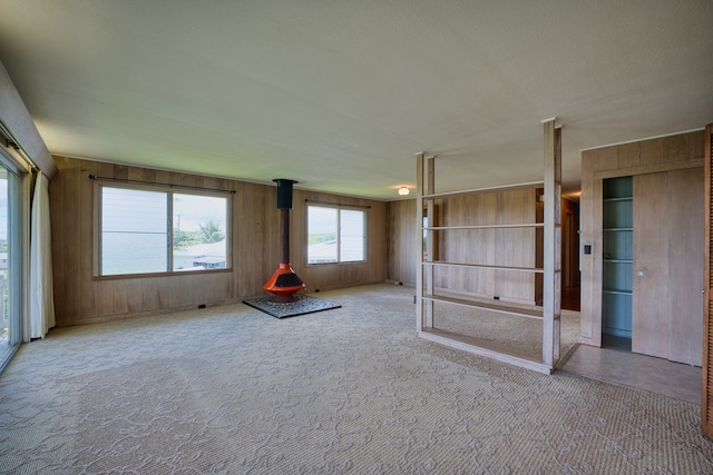 spare room with wood walls, light colored carpet, and a wood stove