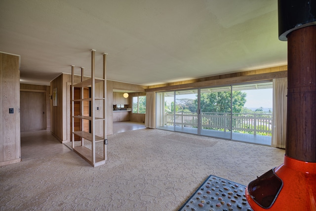 unfurnished living room with plenty of natural light, a wood stove, wooden walls, and carpet flooring