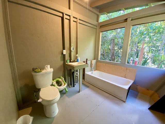 bathroom with concrete floors, a garden tub, and toilet