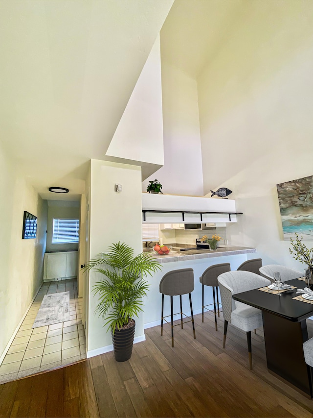 kitchen with a high ceiling, a peninsula, a kitchen breakfast bar, and wood finished floors