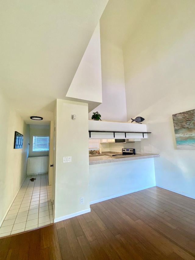 kitchen featuring a peninsula, light countertops, stainless steel electric range, light wood-type flooring, and backsplash