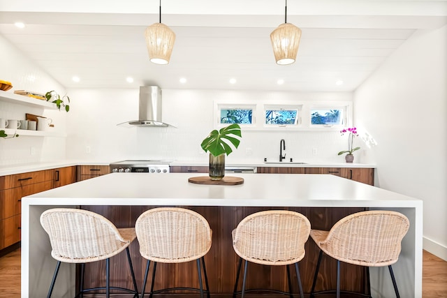 kitchen featuring a spacious island, a sink, light countertops, wall chimney range hood, and open shelves