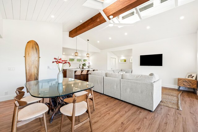 living room featuring beam ceiling, light hardwood / wood-style floors, a skylight, sink, and high vaulted ceiling