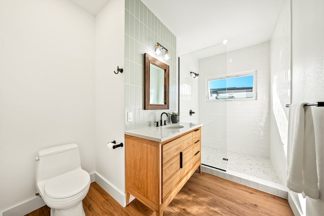 bathroom featuring wood-type flooring, toilet, a tile shower, and vanity