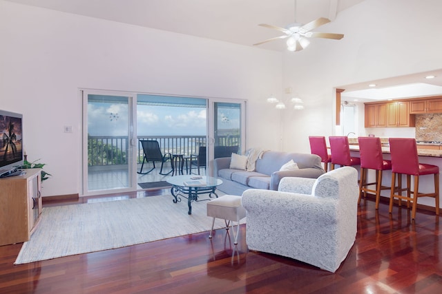 living room with a towering ceiling, dark wood-type flooring, ceiling fan, and beam ceiling