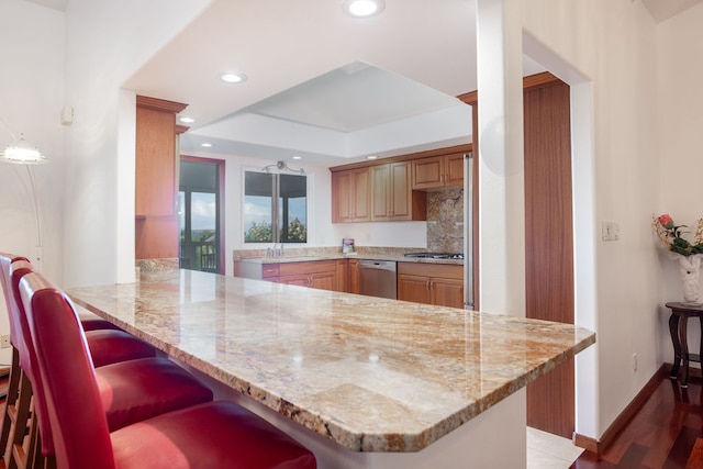 kitchen featuring kitchen peninsula, light stone counters, a kitchen breakfast bar, and dark hardwood / wood-style floors