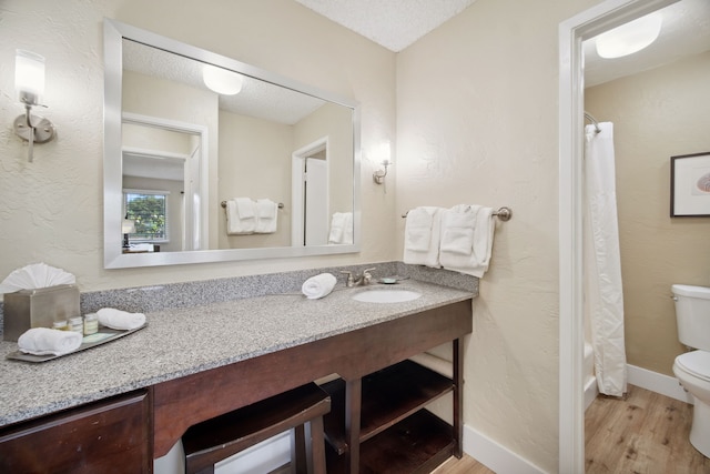 bathroom with wood-type flooring, toilet, vanity, and a textured ceiling