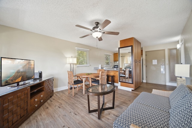 living room featuring light wood-type flooring, a textured ceiling, and ceiling fan