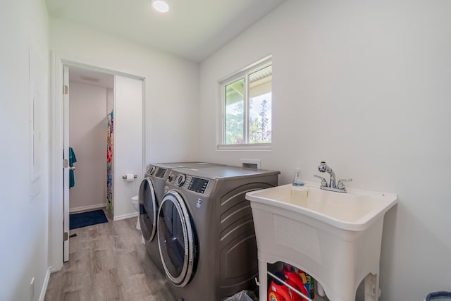 clothes washing area with light hardwood / wood-style flooring, washing machine and dryer, and sink