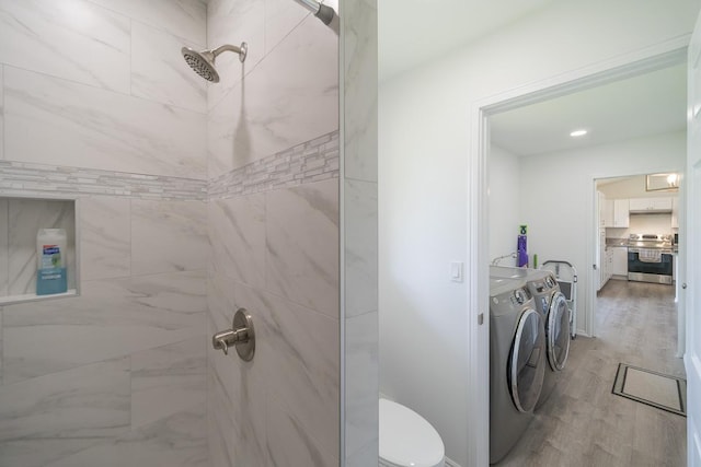 full bathroom featuring washing machine and dryer, tiled shower, toilet, and wood finished floors