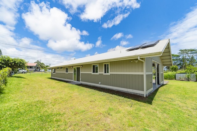 rear view of house featuring metal roof, a yard, solar panels, and fence