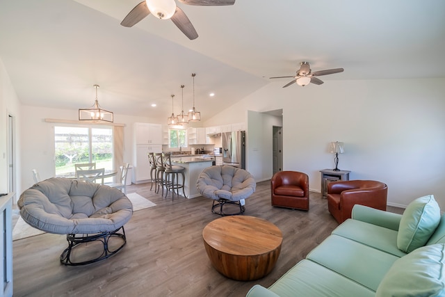 living room with high vaulted ceiling, hardwood / wood-style floors, ceiling fan with notable chandelier, and sink