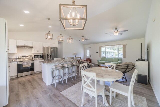 dining area with ceiling fan with notable chandelier, vaulted ceiling, and light hardwood / wood-style flooring