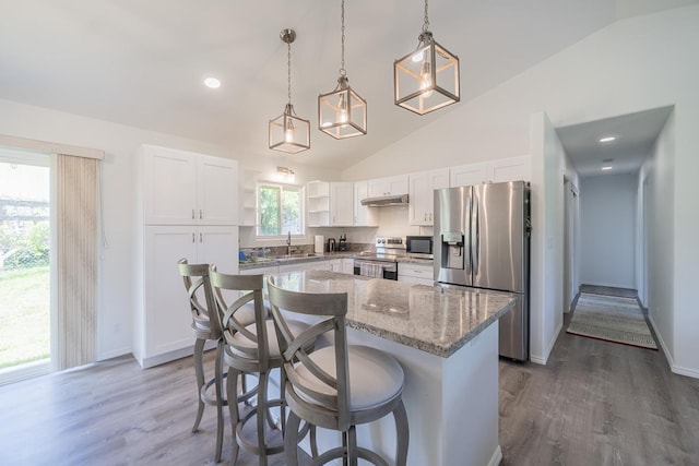 kitchen with white cabinets, appliances with stainless steel finishes, a kitchen breakfast bar, light stone counters, and under cabinet range hood