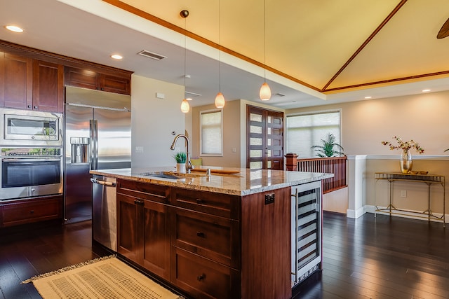 kitchen featuring an island with sink, hanging light fixtures, built in appliances, dark hardwood / wood-style floors, and light stone countertops