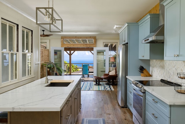 kitchen featuring wood-type flooring, sink, light stone countertops, appliances with stainless steel finishes, and a center island with sink