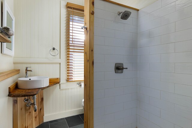 bathroom with wood walls, tile patterned floors, toilet, sink, and tiled shower