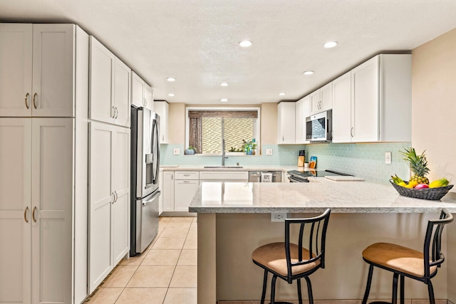 kitchen featuring white cabinets, kitchen peninsula, a breakfast bar, and stainless steel appliances