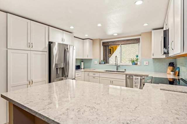 kitchen with stainless steel appliances, light stone counters, kitchen peninsula, sink, and white cabinetry