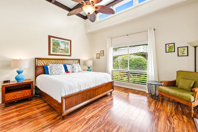 bedroom with beam ceiling, ceiling fan, a high ceiling, and hardwood / wood-style flooring