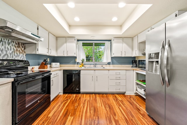 kitchen with black appliances, light hardwood / wood-style floors, and a raised ceiling