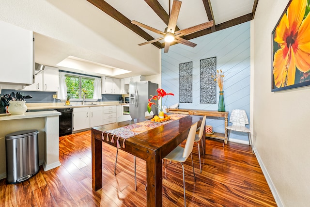 dining room with ceiling fan, dark wood-type flooring, wooden walls, sink, and lofted ceiling with beams