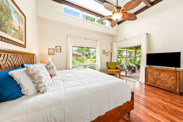 bedroom with a towering ceiling, access to outside, ceiling fan, hardwood / wood-style flooring, and beamed ceiling