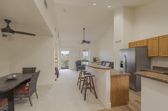 kitchen with stainless steel refrigerator with ice dispenser, a ceiling fan, a kitchen island, high vaulted ceiling, and a kitchen breakfast bar