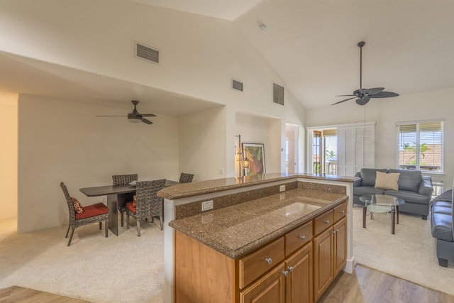 kitchen with brown cabinetry, visible vents, open floor plan, and dark stone countertops