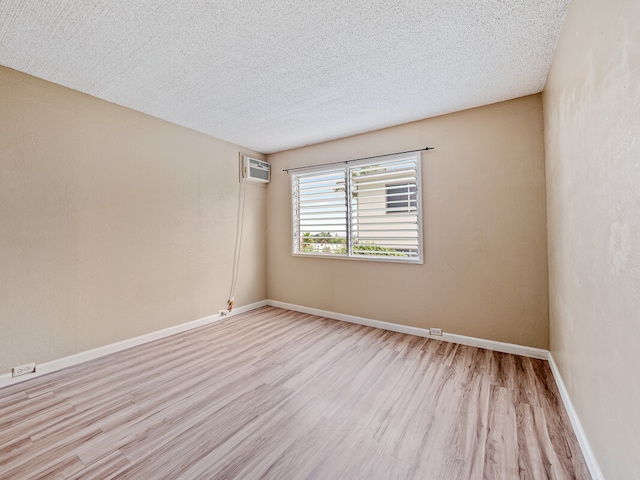 empty room featuring a textured ceiling, a wall mounted air conditioner, and light hardwood / wood-style floors