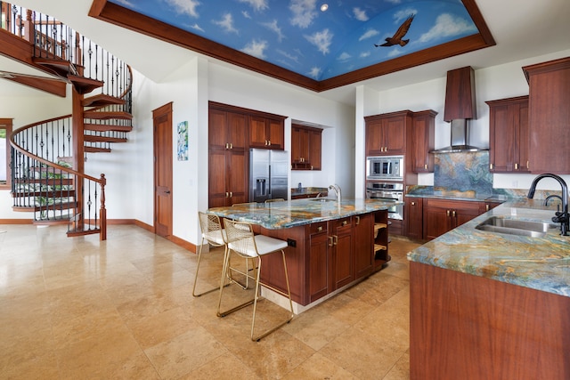 kitchen featuring sink, wall chimney range hood, dark stone countertops, an island with sink, and appliances with stainless steel finishes